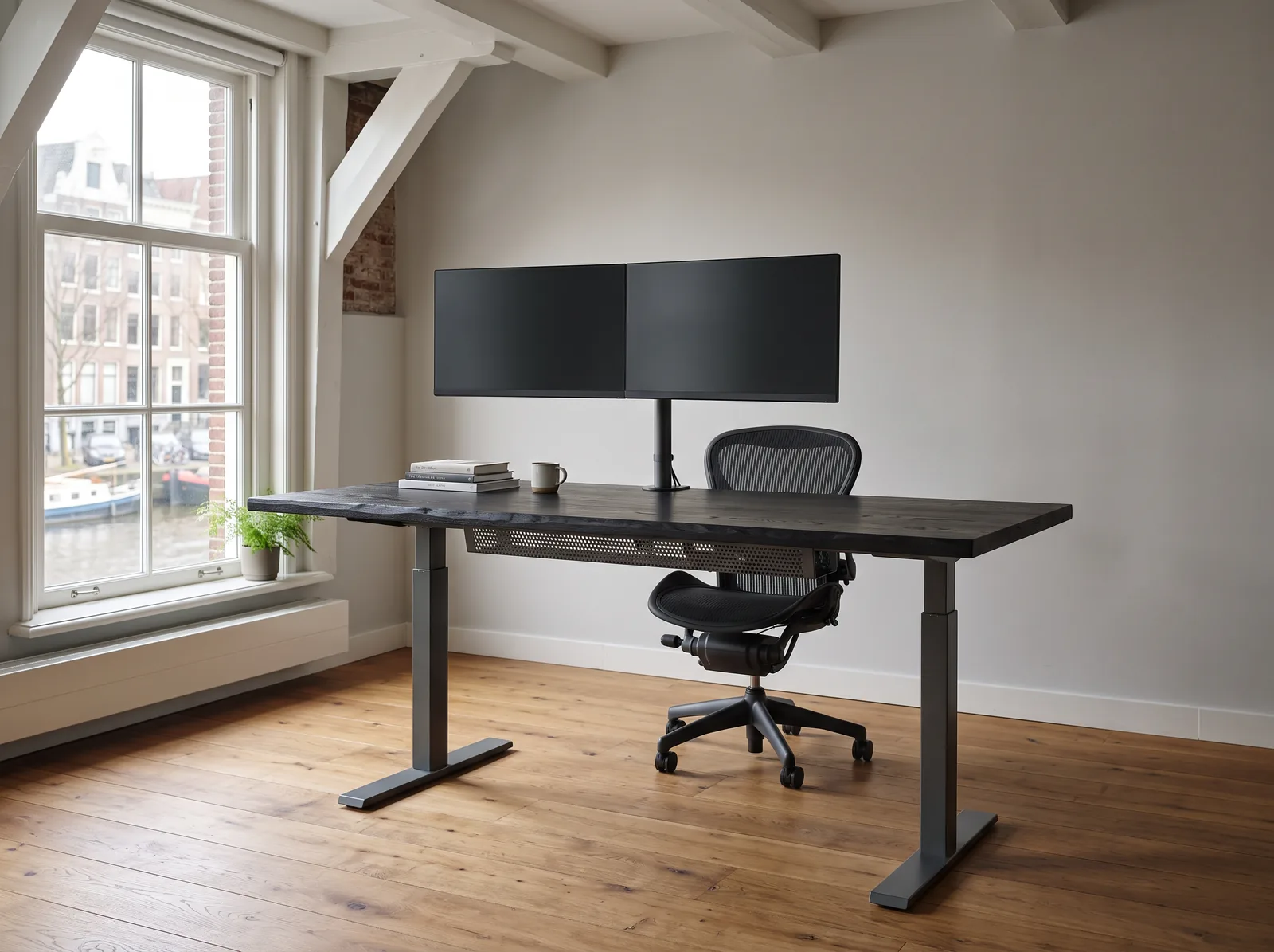 Ein Apex Pro in Räucheresche auf Graphit-Rahmen unter den Balken eines Grachtenhauses, zwei Displays bündig auf einer Säule und eine perforierte Kabelwanne unter der Platte.